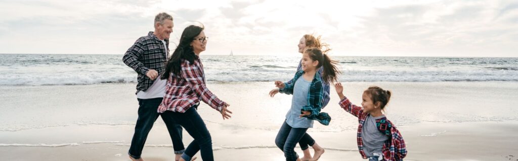 Família correndo de mãos dadas na praia, com expressão de alegria e liberdade ao representar a proteção do patrimônio da sua família com segurança.