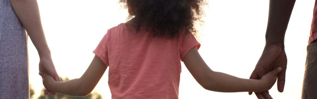 Criança de mãos dadas com dois adultos ao entardecer, simbolizando união e proteção patrimonial. Holding familiar e empresarial: quando vale a pena criar uma?